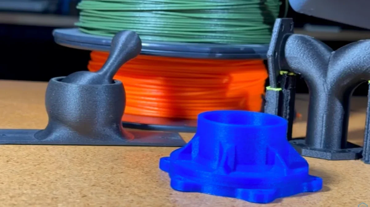 3D printed objects in black and blue with spools of green and orange filament in the background.