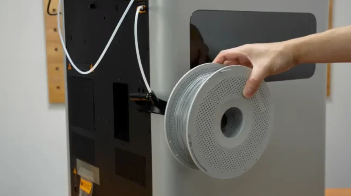 Hand loading filament spool onto Bambu Lab H2D 3D printer with integrated cable management.