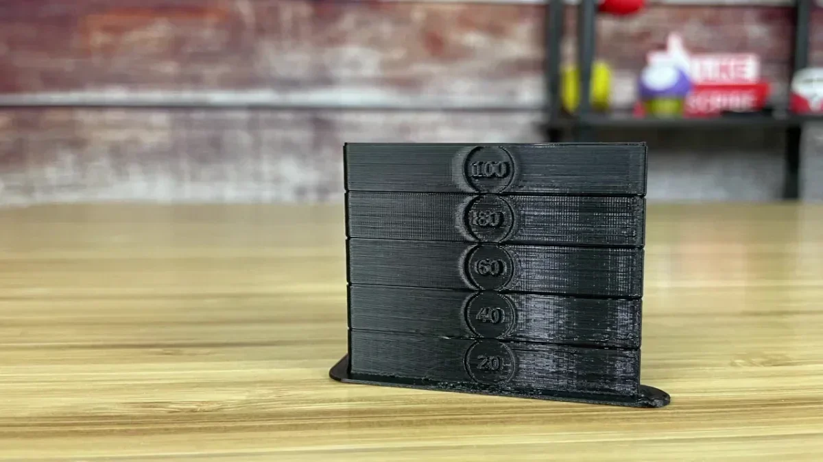 Black 3D printed speed tower with labeled sections: 100, 80, 60, 40, 20 mm/s on a wooden surface.